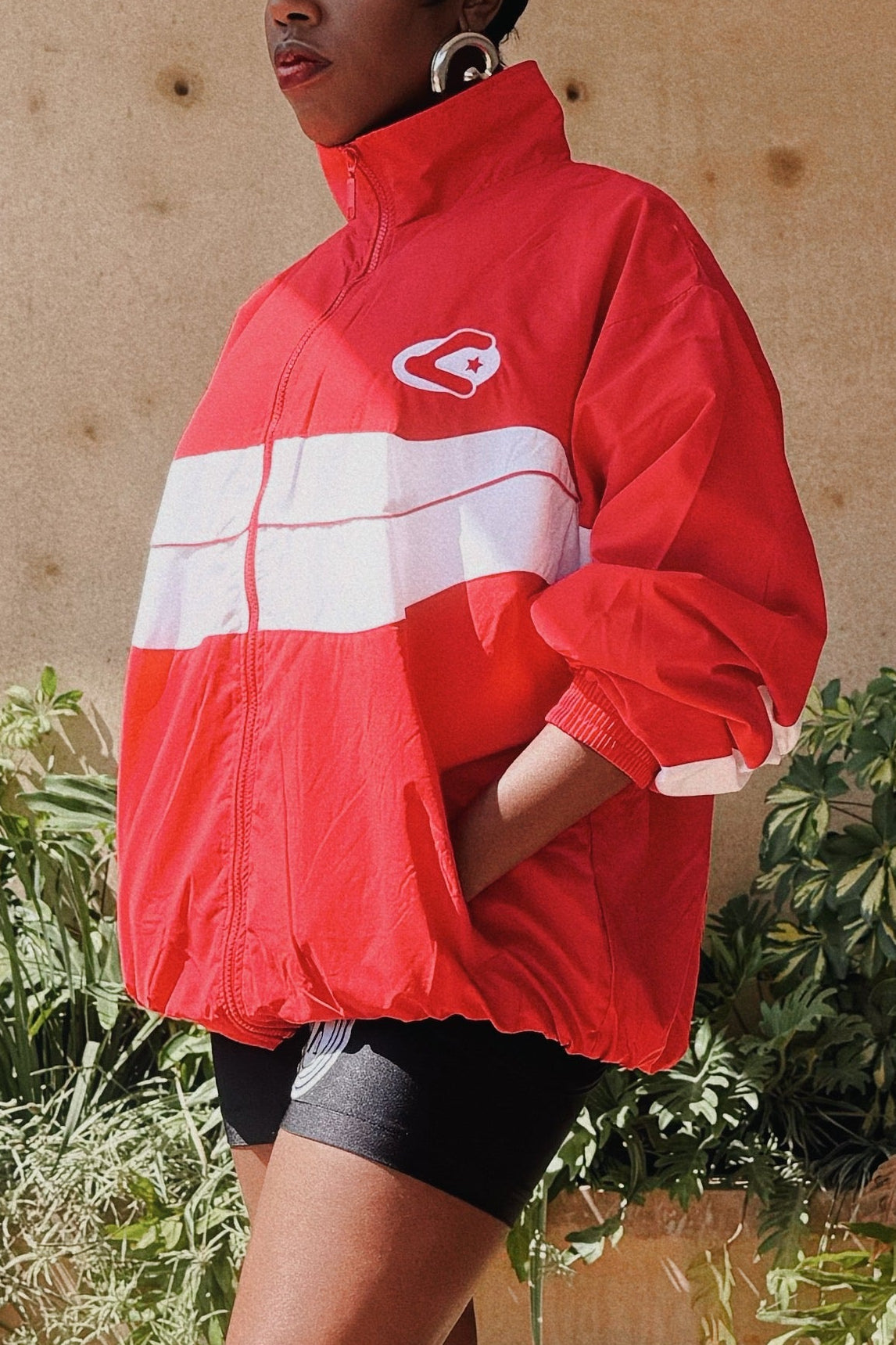 Person wearing a red raincoat on a wooden deck with plants and a building in the background